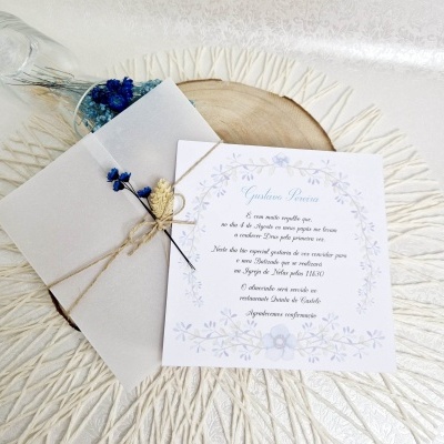 Convite de casamento com decoração floral azul e envelope bege sobre superfície branca texturizada
