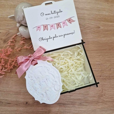 Caixa com laço rosa, anjo decorativo branco e cartão do batizado sobre mesa de madeira clara