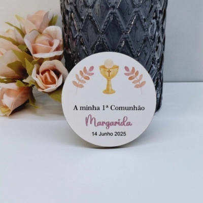 Etiqueta redonda branca com cálice dourado e texto sobre comunhão, junto a vaso preto e flores cor de rosa