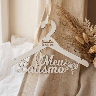 Cabide branco decorativo com texto Meu Batismo, nome e data, pendurado em tecido bege com flores secas ao lado