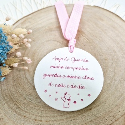 Ornamento redondo branco com texto e desenho, fita rosa e flores secas sobre base de madeira