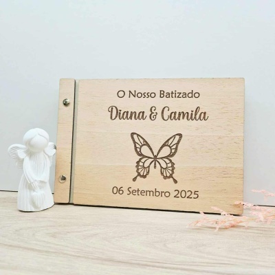 Album de madeira clara com gravação de batizado ao lado de figura branca de anjo