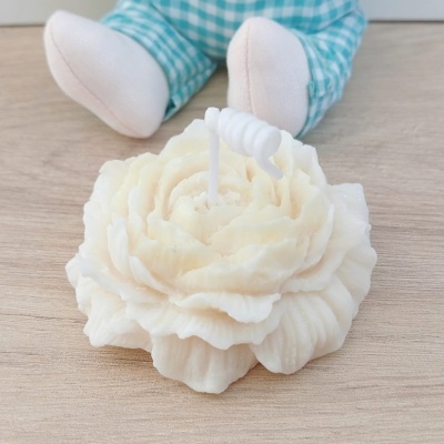 Vela branca em forma de flor sobre superfície de madeira com roupa xadrez azul ao fundo