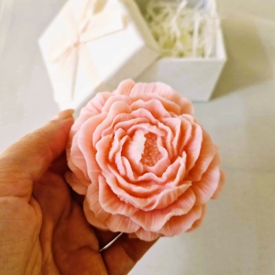 Vela decorativa em forma de flor cor-de-rosa com pétalas e caixa branca ao fundo