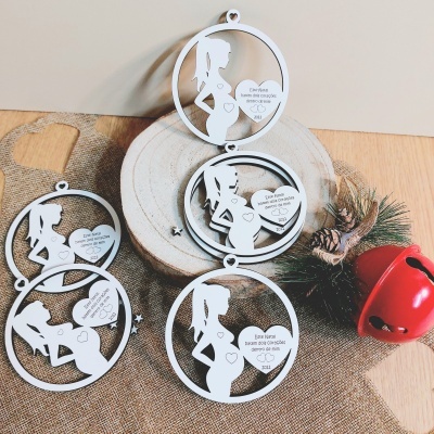 Enfeites brancos de madeira com silhuetas de grávidas e corações com texto, em cenário rústico sobre tecido castanho com sino vermelho