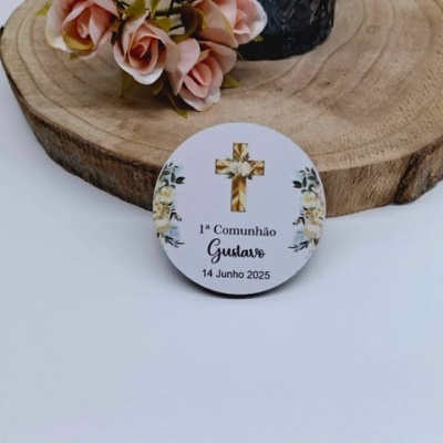 Botão branco decorativo para 1ª Comunhão com cruz dourada e flores, sobre base de madeira e flores cor de rosa