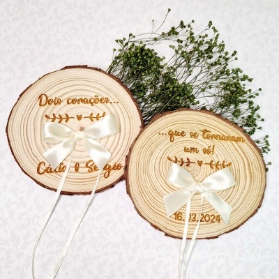 Apoios de alianças redondos em madeira com laços brancos e inscrições gravadas a laser, com flores secas ao fundo