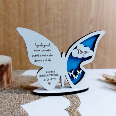 Objeto decorativo borboleta branca com recorte azul e texto em português, sobre base e mesa branca