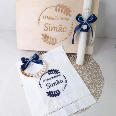 Conjunto de batismo com caixa de madeira, vela branca, toalha e concha decorativa com laços azuis.