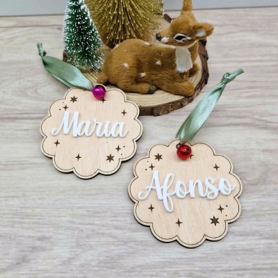 Dois enfeites de madeira com nomes Maria e Afonso, fitas verdes e sinos, ao lado de veado decorativo e mini árvores.
