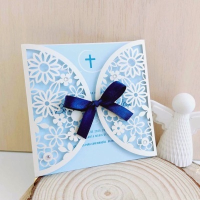 Convite azul claro com decorações florais brancas e laço azul, junto a anjo decorativo branco