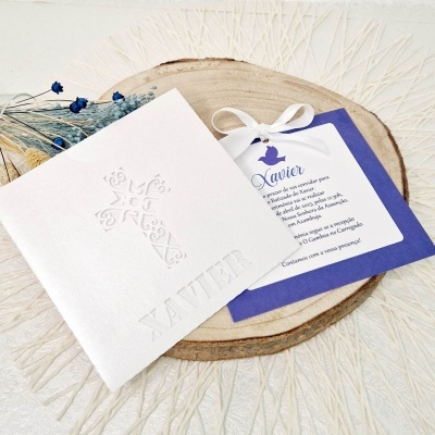 Convite de batizado branco com cruz em relevo e cartão azul com texto sobre tábua de madeira