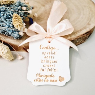 Etiqueta decorativa com mensagem em dourado e laço cor de rosa sobre madeira e flores secas