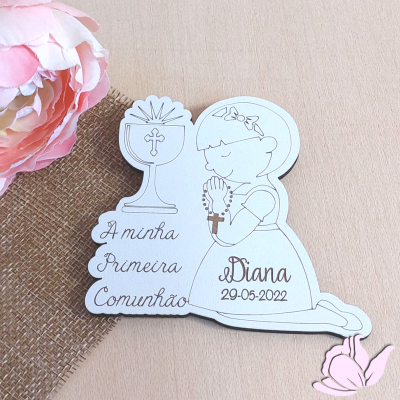 Figura de madeira recortada com desenho e texto sobre Primeira Comunhão, com flor rosa ao lado.