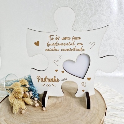 Peça de puzzle branca em madeira com texto gravado e coração recortado, sobre tronco de madeira, com flores secas.