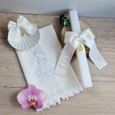 Conjunto de toalha branca bordada com concha, vela com laço e orquídea rosa sobre madeira clara