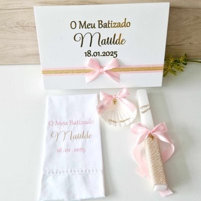 Conjunto de batizado com toalha bordada, concha decorativa e vela com laço rosa.