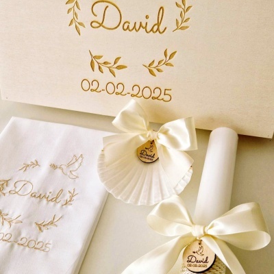 Conjunto de cerimónia com toalha branca bordada, concha com laço e vela enrolada com fita creme e medalhas decorativas