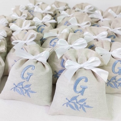 Sacos de tecido bege com laços brancos e monograma 'G' bordado azul
