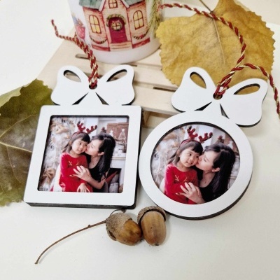 Dois porta-fotos em madeira branca com fotografias de mulher e criança com laços vermelhos