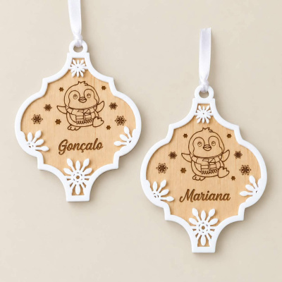 Ornamentos decorativos de madeira clara com bordas brancas, desenhos de pinguim e nomes Gonçalo e Mariana.