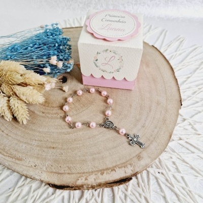 Terço cor de rosa e caixa decorativa para primeira comunhão junto a flores secas sobre base de madeira