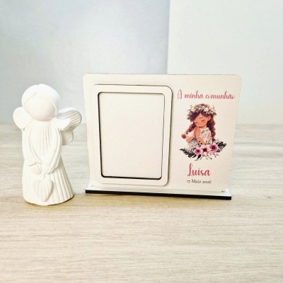 Estátua de anjo branca junto a moldura com ilustração e texto de comunhão num fundo de madeira clara