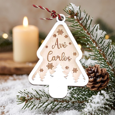 Ornamento de Natal em forma de árvore com texto Avô Carlos pendurado em ramo de pinheiro com neve e pinha ao lado