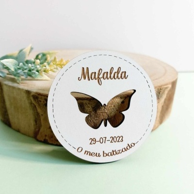 Etiqueta branca redonda com recorte de borboleta e texto em castanho sobre tronco de madeira
