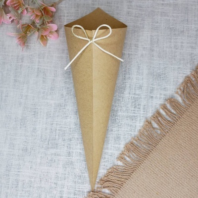 Cone de papel kraft com fita branca sobre toalha de linho e tecido cru com flores cor-de-rosa