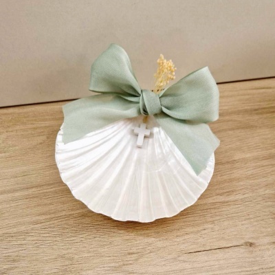 Concha branca com laço verde claro e pendente de cruz sobre madeira.