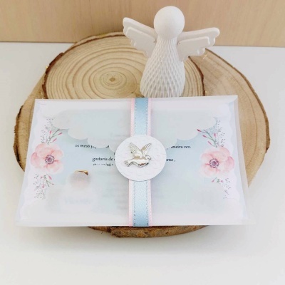 Brinde para batizado com embalagem branca translúcida e decoração de flores e anjo sobre base de madeira