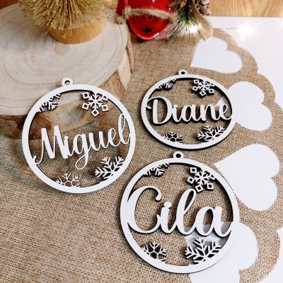 Ornamentos de Natal brancos em madeira com nomes e flocos de neve sobre tecido castanho