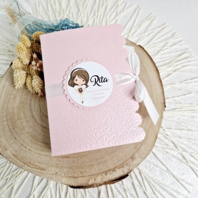 Convite rosa de comunhão com fita branca e etiqueta de menina, em prato de madeira com flores secas