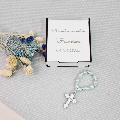 Caixa branca personalizada com texto de comunhão, flores secas azuis e brancas e terço perolado azul com crucifixo em fundo cinza