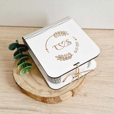 Convite dobrável branco com letras douradas e decoração de ramos sobre base de madeira com raminho verde