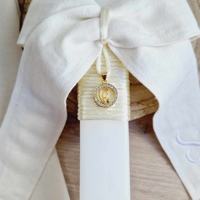 Vela decorativa branca com laço e medalha pendurada sobre base de madeira