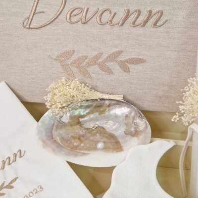 produtos bordados em tom bege com nome Devann e prato de concha perolado