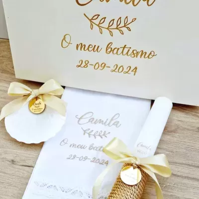 Conjunto para batismo com toalha branca, caixa, concha e vela decorativa, com texto em dourado e dourado claro.
