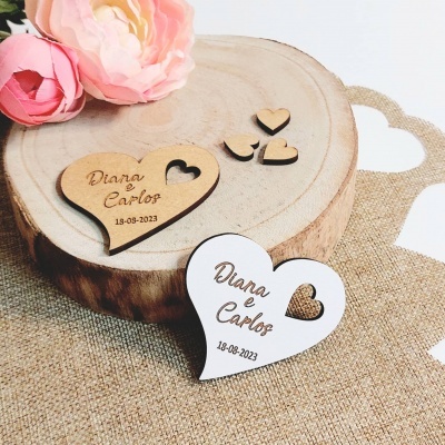 Dois corações em madeira gravados, um natural e um branco, sobre tronco de madeira com flores e tecido bege