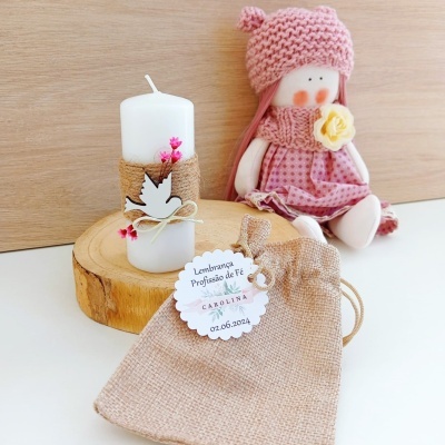 vela branca decorada com juta e pomba de madeira, bolsa de juta com etiqueta e boneca de pano cor-de-rosa