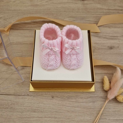 Sapatinhos de bebé cor-de-rosa em malha com laços, numa caixa dourada sobre madeira clara