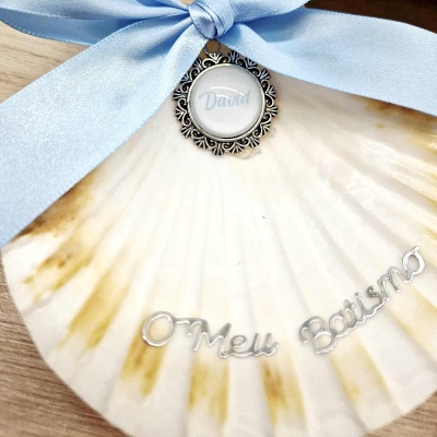 Concha decorativa branca com laço azul e texto prateado de batismo