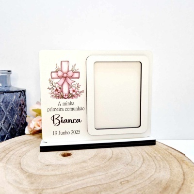 Moldura branca com suporte preto com cruz cor-de-rosa e texto relacionado com primeira comunhão