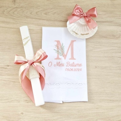 Conjunto de batismo com vela, toalha bordada e concha decorativa sobre superfície de madeira clara