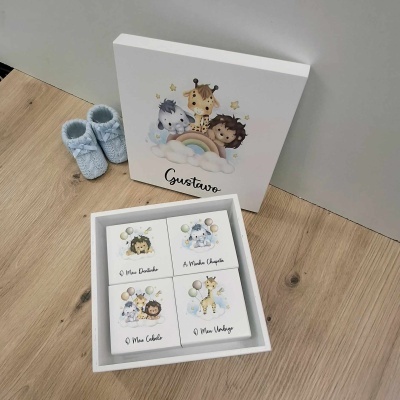 Caixas em madeira brancas com ilustrações de animais e o nome Gustavo, junto a sapatilhas azuis para bebé no chão de madeira