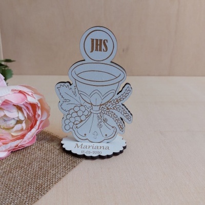 Figura decorativa em madeira clara de cálice com inscrições e flores ao lado