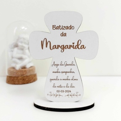 Produto em forma de cruz branca com texto sobre batizado e figura sob cúpula de vidro no fundo