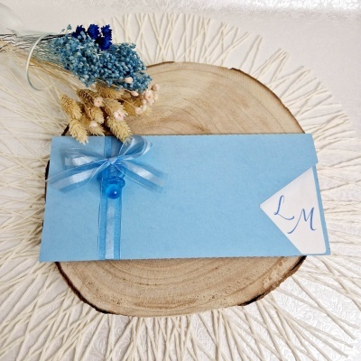 Envelope azul decorado com fita e botão azuis sobre base de madeira com flores secas