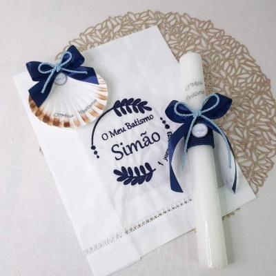 Conjunto de batismo com vela branca, toalha branca bordada e concha decorativa com laços azuis